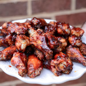 hand holding a plate of smoked chicken wings with BBQ sauce
