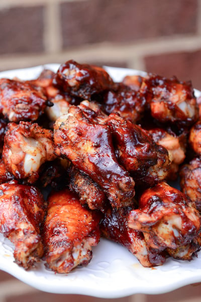 hand holding a plate of smoked chicken wings with BBQ sauce