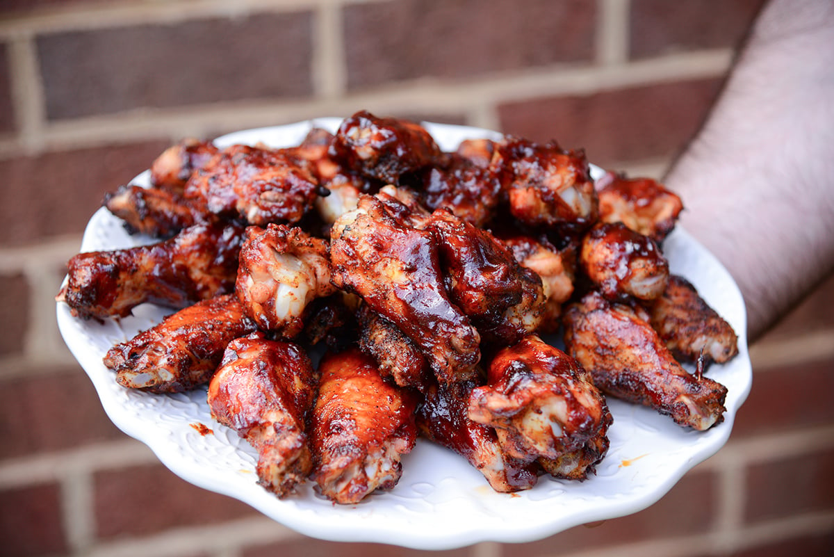 hand holding a plate of smoked chicken wings with BBQ sauce