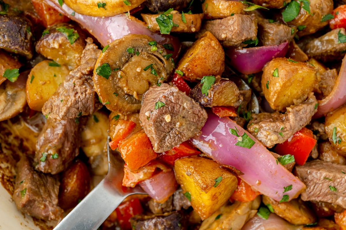 overhead shot of serving spoon of steak and potato skillet