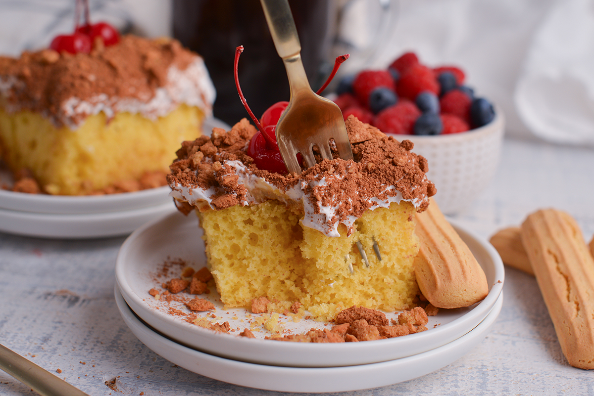 straight on shot of fork digging into slice of tiramisu poke cake