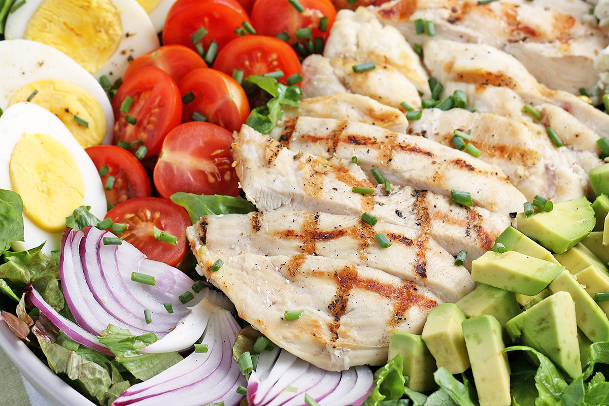 close up of sliced chicken, avocado, red onion, tomato and boiled eggs