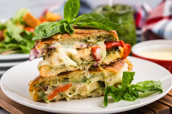 straight on shot of Italian chicken panini halves on plate topped with basil