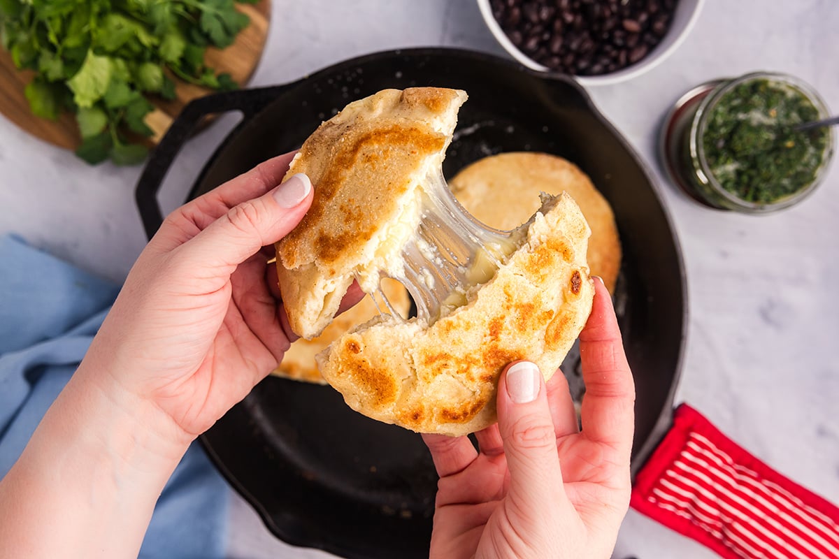 hands breaking easy arepas con queso in half