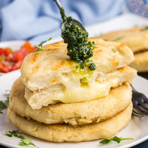 spoon adding chimichurri sauce to stack of arepas