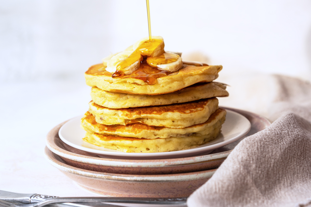 straight on shot of syrup pouring onto stack of pancakes
