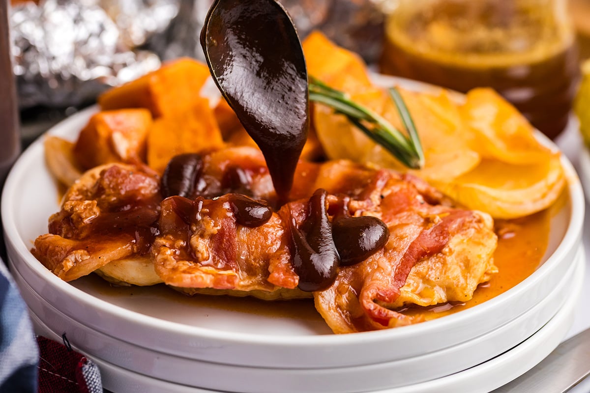 spoon adding bbq sauce to plate of chicken and sweet potatoes