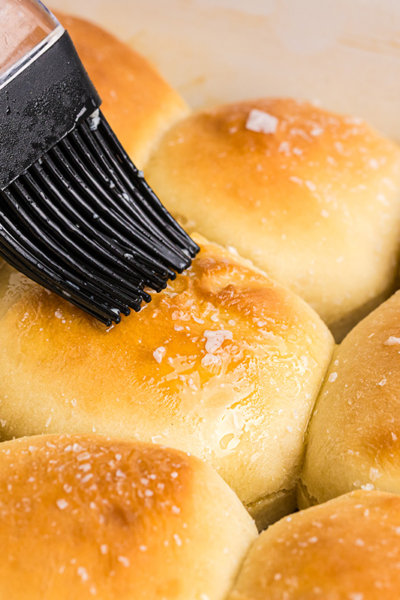 angled shot of butter brushed onto pan of dinner rolls