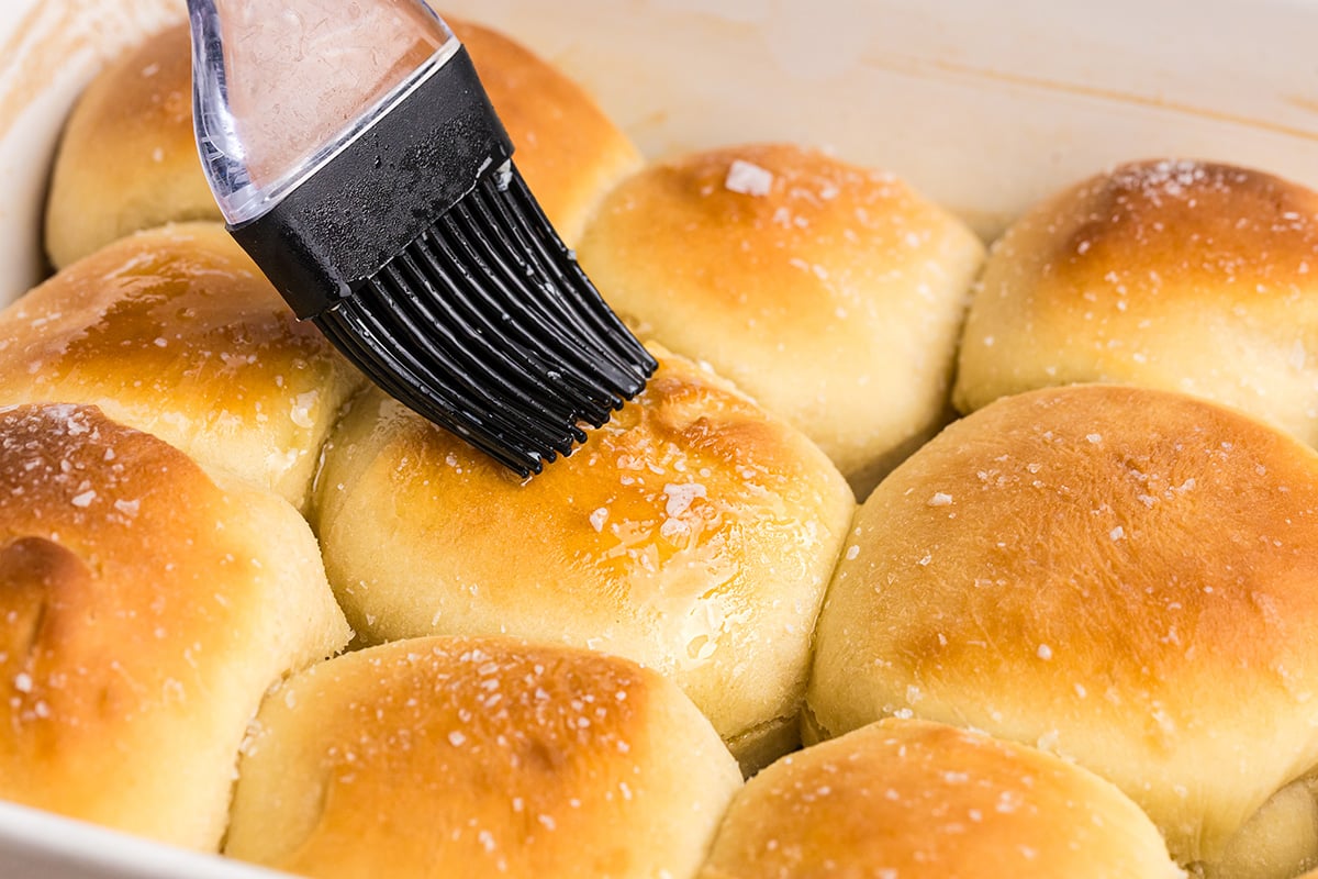 angled shot of butter brushed onto pan of homemade dinner rolls