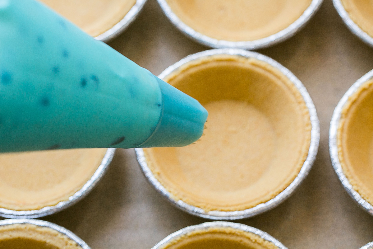 piping bag held over mini graham cracker crusts