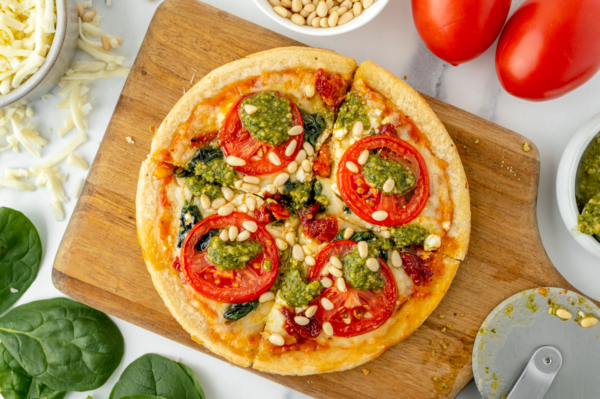 sliced tomato pesto pizza on cutting board