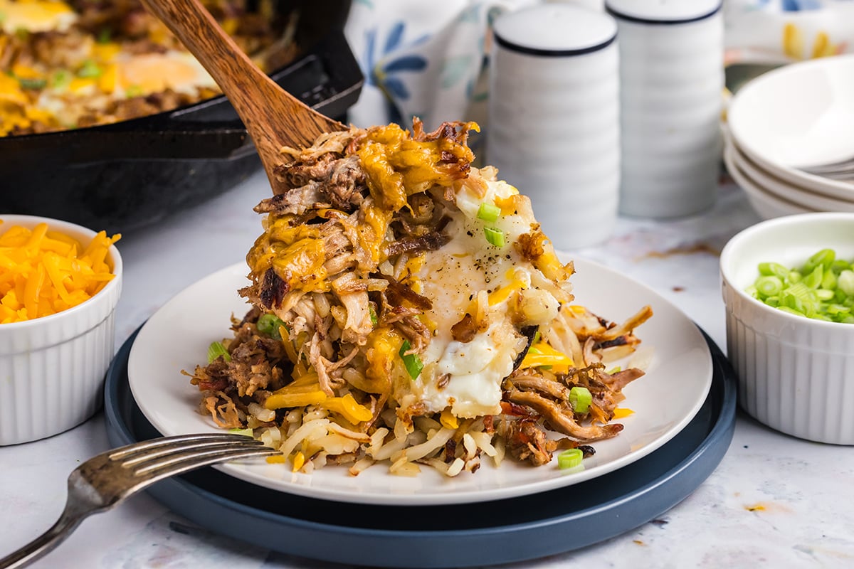 angled shot of wooden spoon adding scoop of bbq pulled pork hash to plate