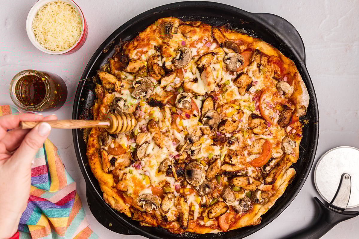 overhead shot of honey drizzled over jerk chicken pizza