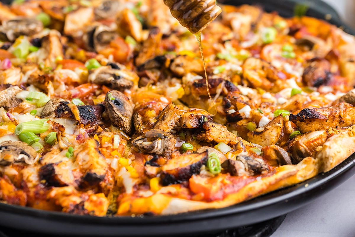 angled shot of honey drizzling over jerk chicken pizza