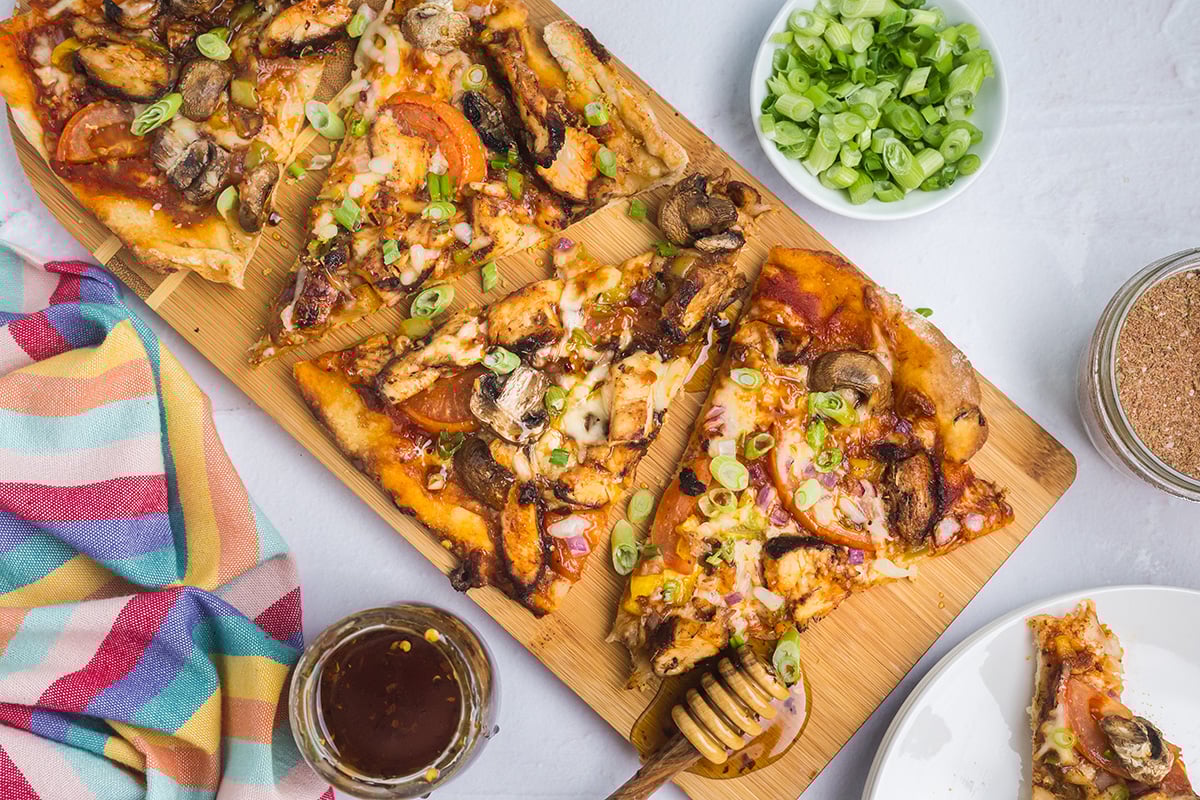overhead shot of slices of jerk chicken pizza on wooden board