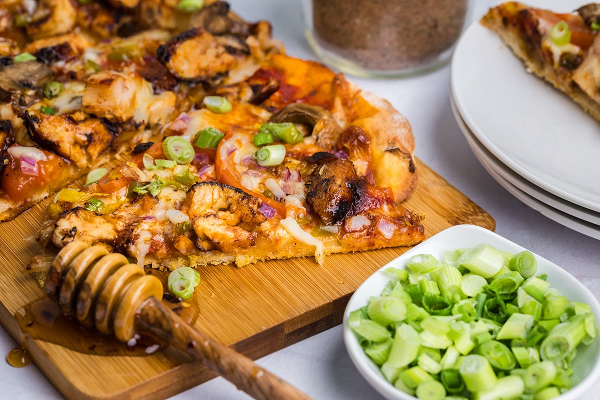 angled shot of slice of jerk chicken pizza on board with honey