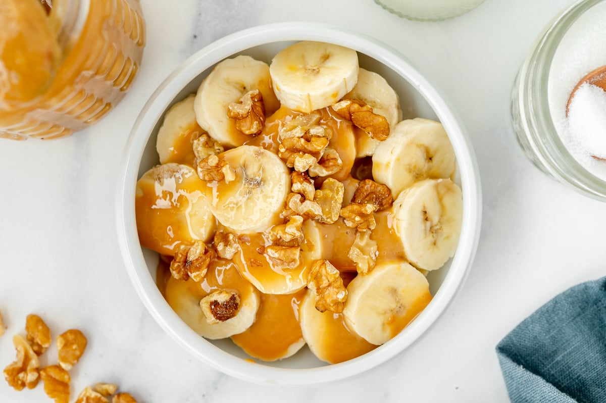 overhead shot of bowl of sliced bananas, walnuts and caramel
