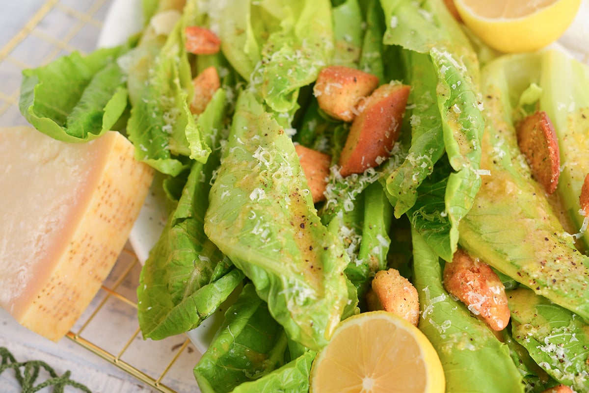 close up of parmesan cheese, leafy greens dressing with a garlic dressing, croutons and freshly ground pepper