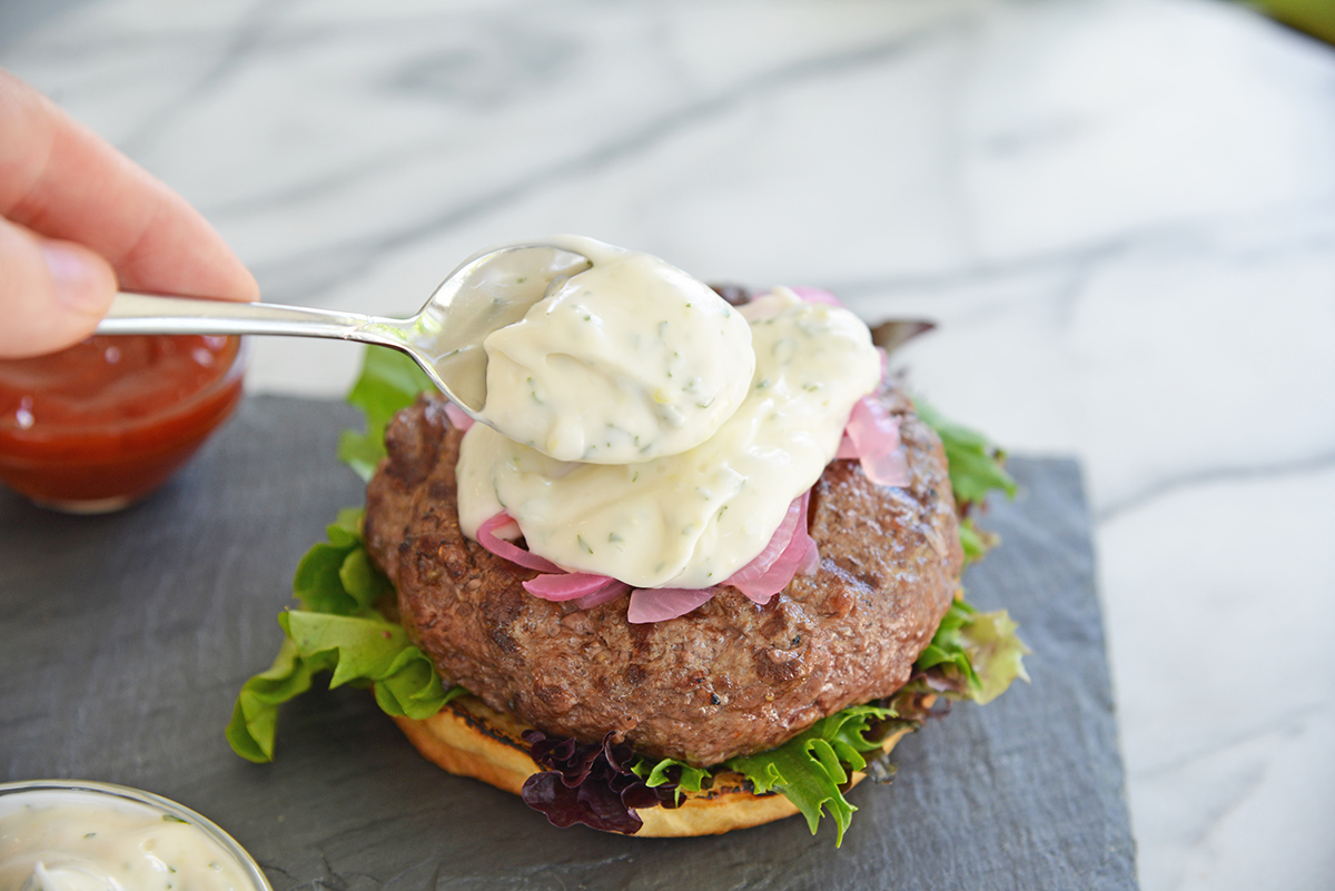 spoon adding tzatziki sauce to burger
