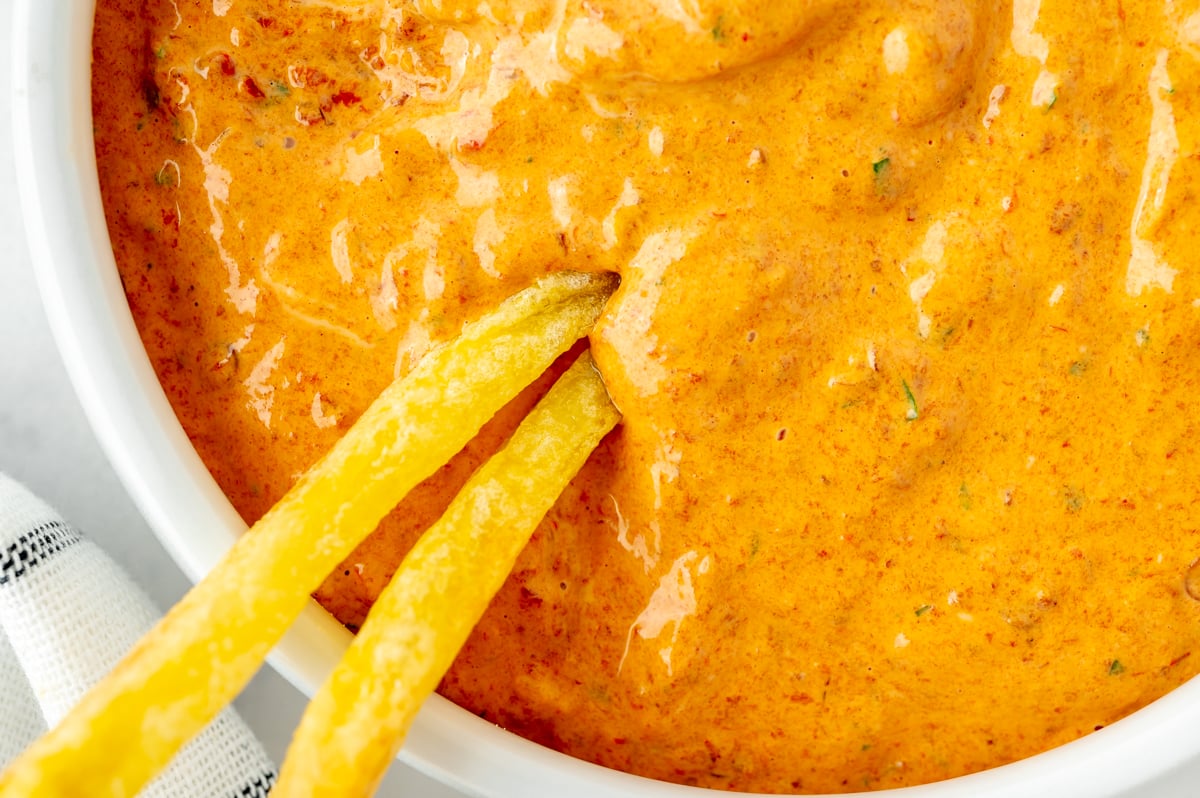 close up of two french fries in bowl of chipotle pepper aioli