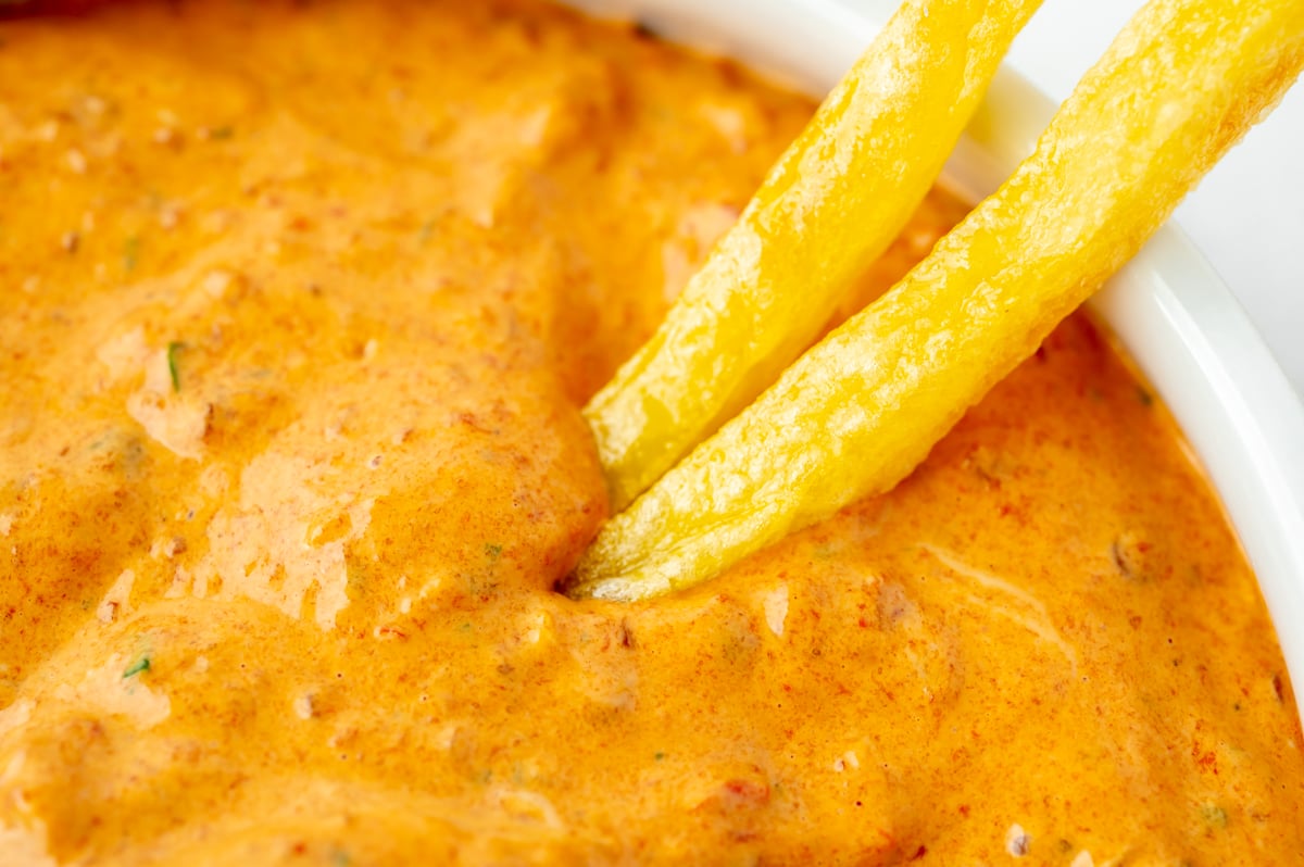 angled shot of two french fries dipping into bowl of chipotle pepper mayo