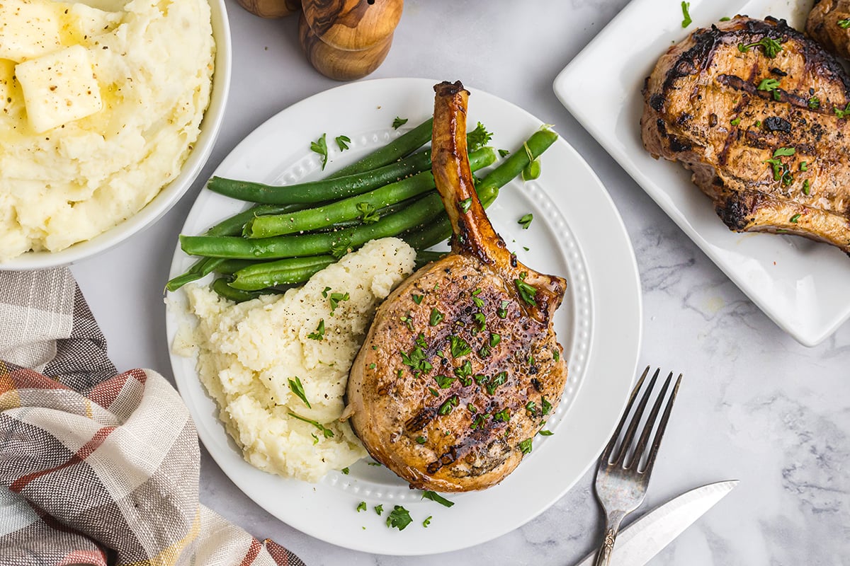 overhead shot of grilled pork chop on plate with green beans and potatoes