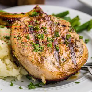 close up angled shot of onion grilled pork chop on plate with potatoes