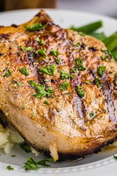 close up angled shot of onion grilled pork chop on plate with potatoes