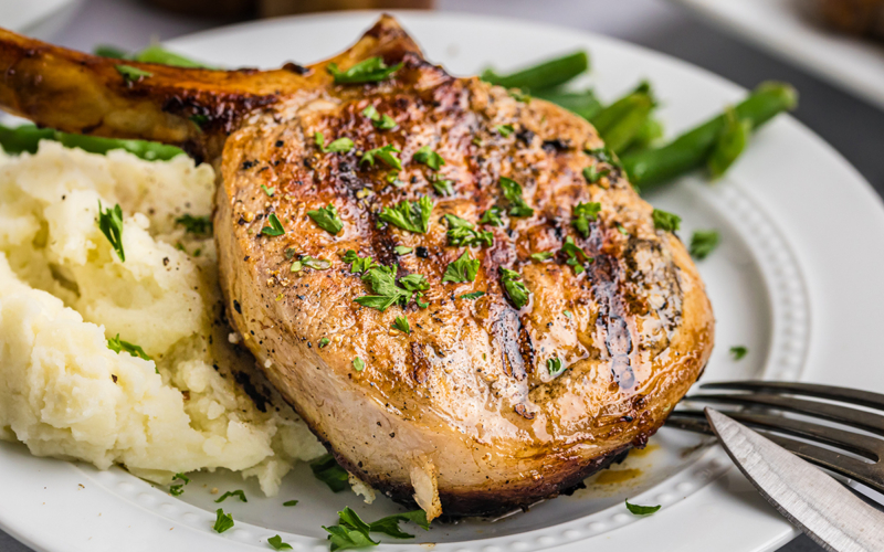 close up angled shot of onion grilled pork chop on plate with potatoes