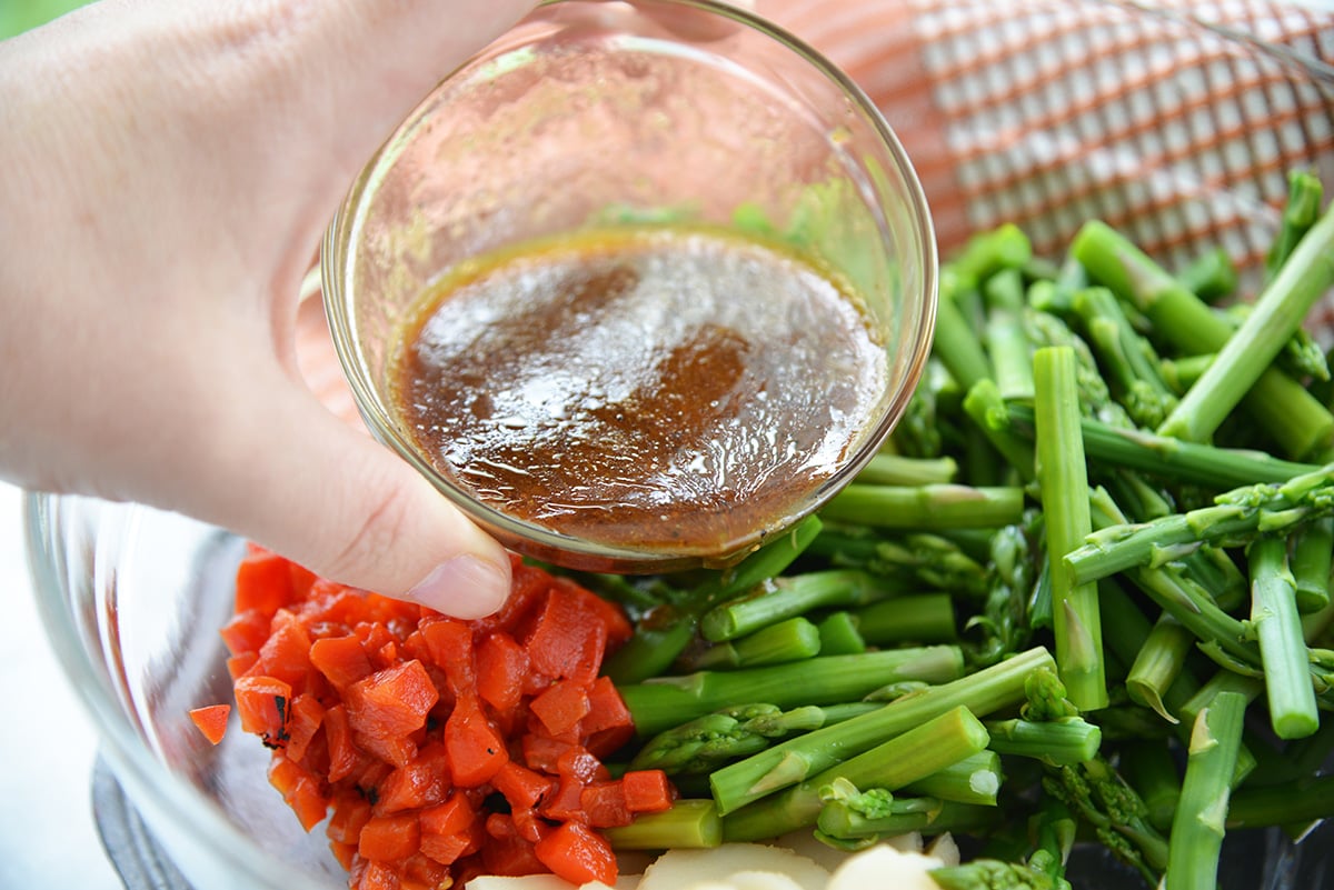 pouring balsamic vinegar dressing on marinated asparagus