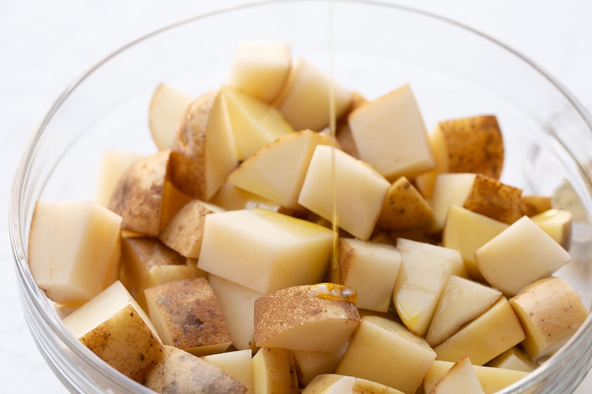 oil pouring into bowl of cubed potatoes