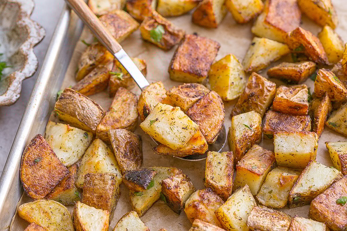 angled sot of spoon scooping ranch potatoes from baking sheet