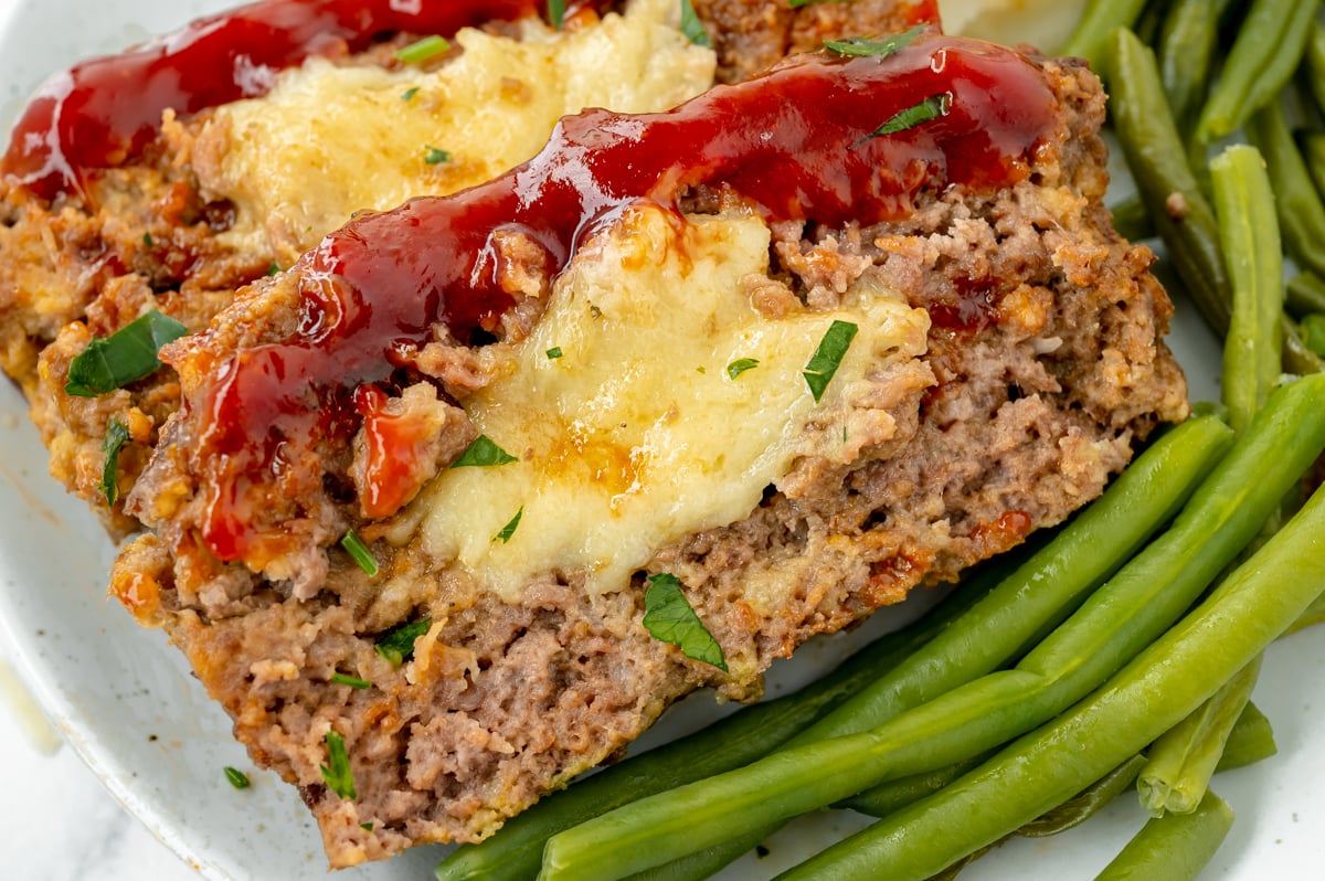 close up angled shot of sliced cheesy meatloaf on plate with green beans