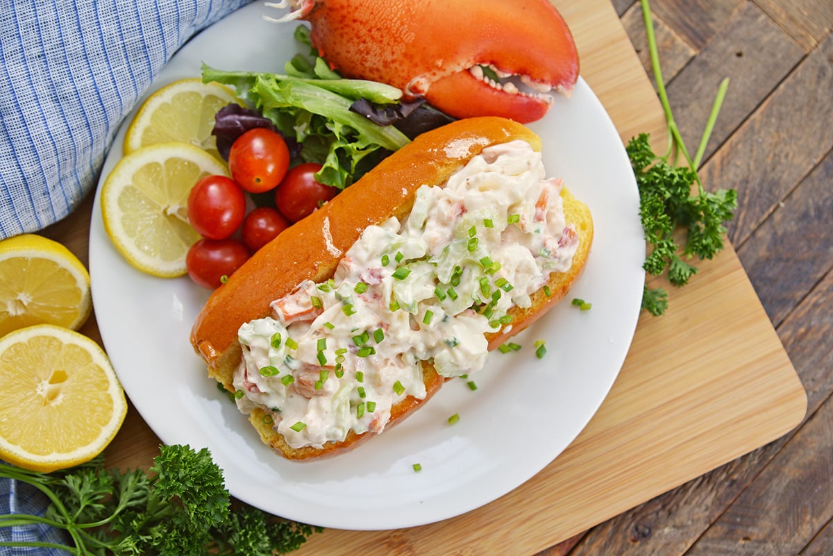 cold lobster roll on a plate with a lobster claw and salad