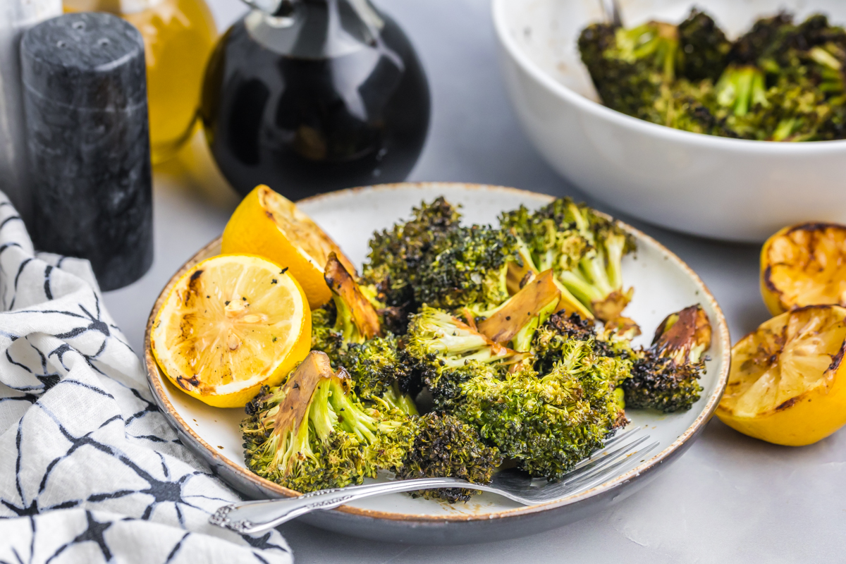 angled shot of plate of grilled broccoli with charred lemon and fork