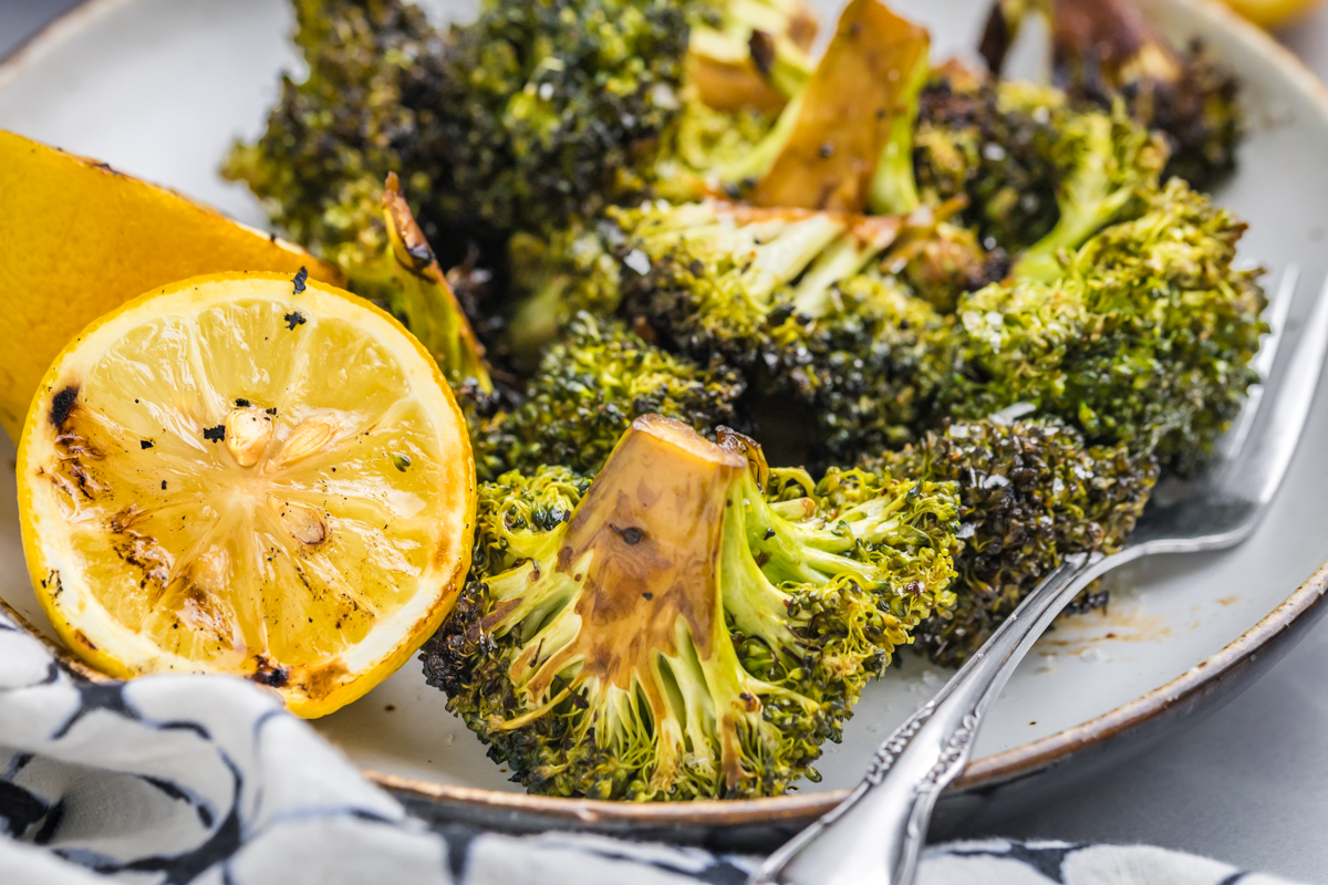 close up angled shot of plate of grilled broccoli with charred lemon and fork