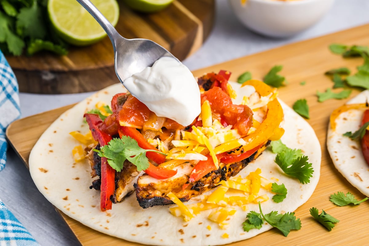 spoon adding sour cream to chicken fajita