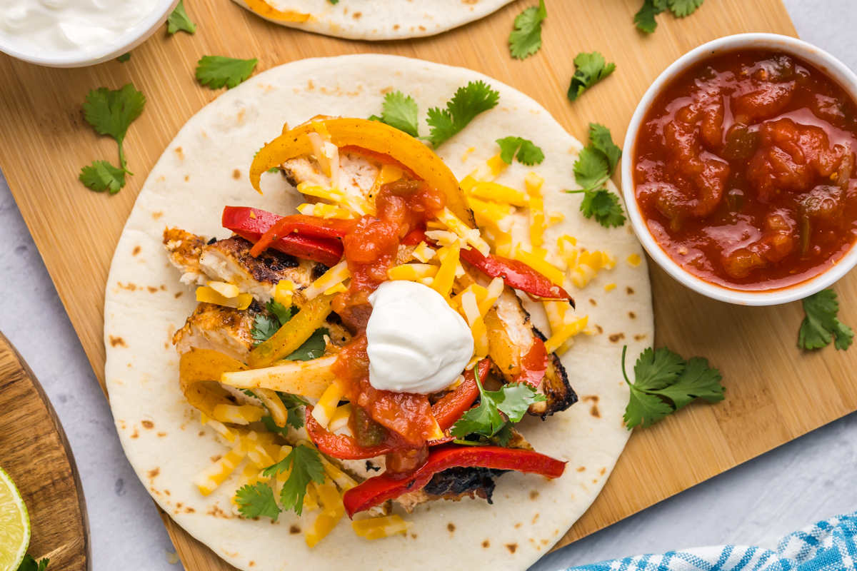 overhead shot of grilled chicken fajita on board with bowl of salsa