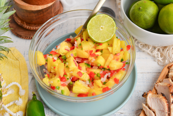 angled shot of pineapple salsa in bowl with spoon and lime