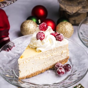 angled shot of slice of cheesecake on plate topped with sugared cranberries