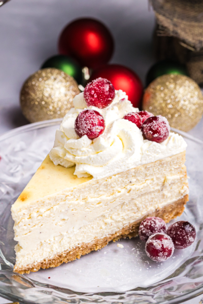 angled shot of slice of cheesecake on plate topped with sugared cranberries
