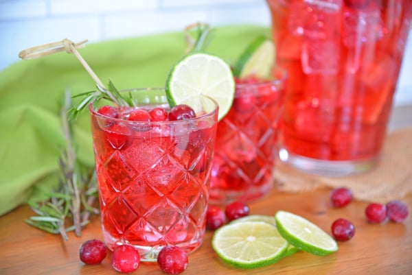 Side view of cocktail glass with cranberries, ice cubes and lime