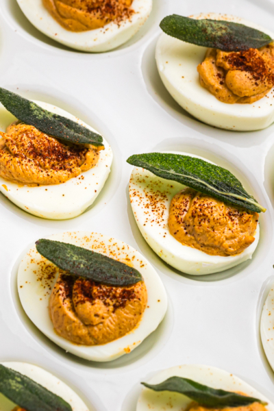 angled shot of platter of deviled eggs topped with sage leaves