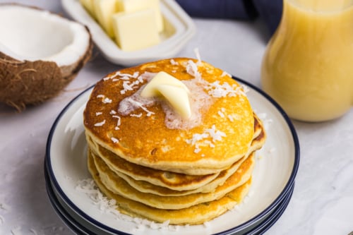 angled shot of stack of pancakes topped with coconut and butter