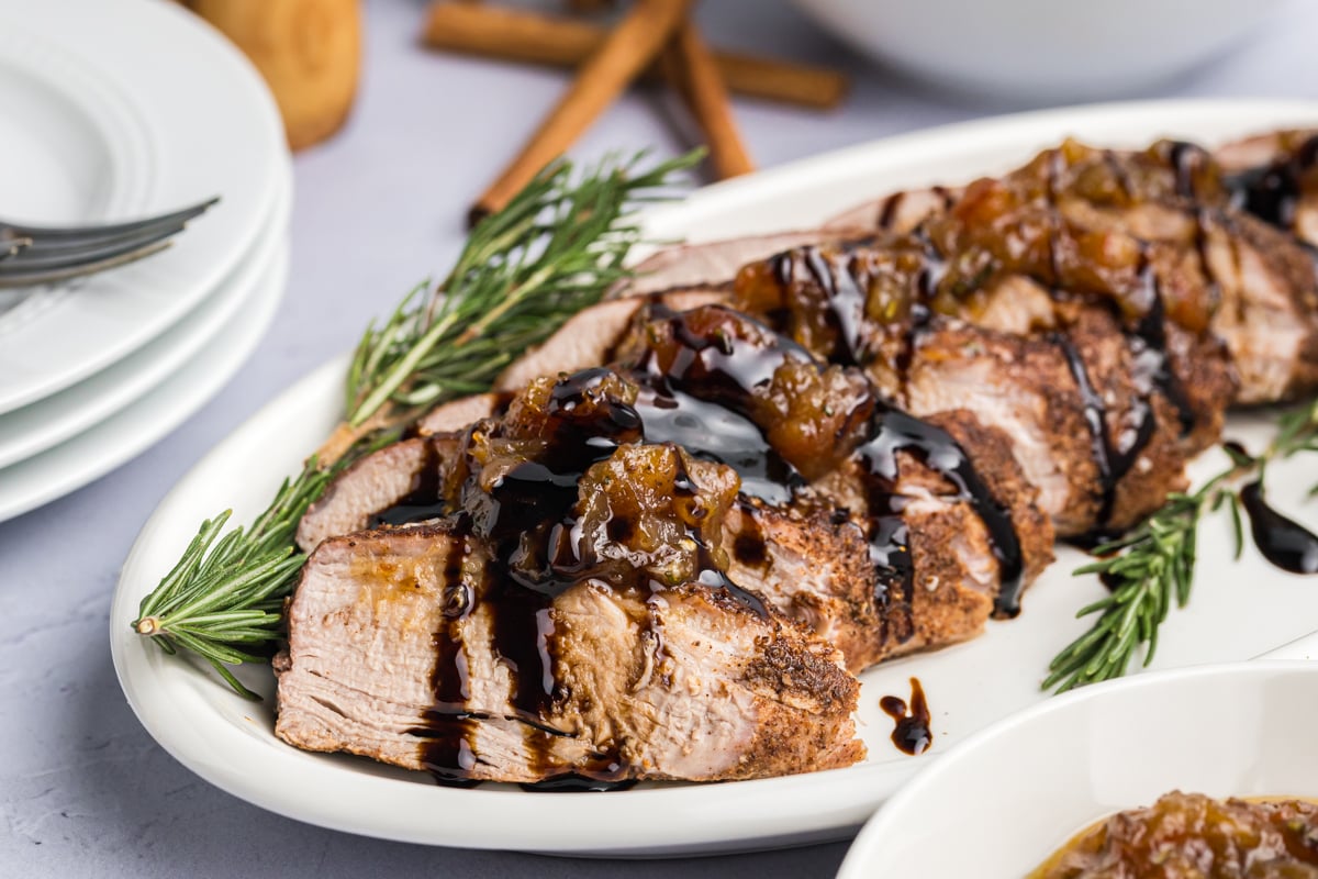 close up angled shot of sliced pork tenderloin on platter with rosemary