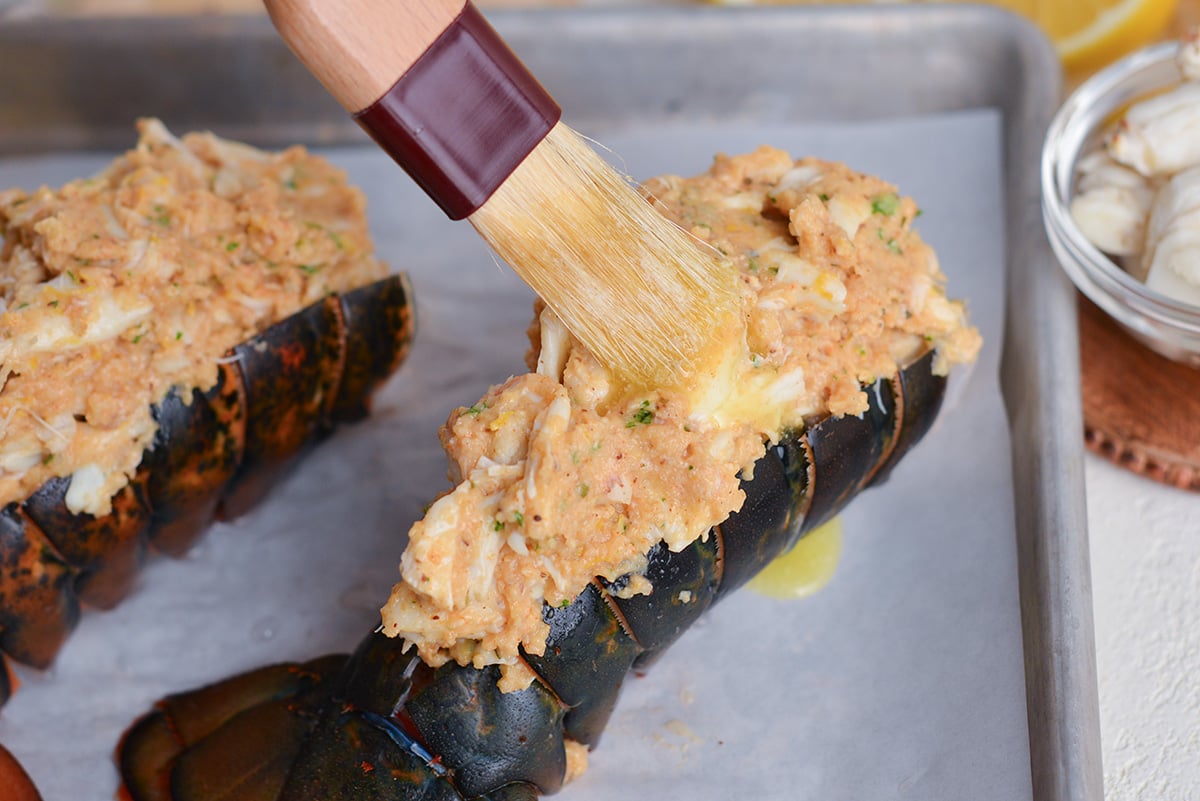 angled shot of brush adding melted butter to stuffed lobster tail