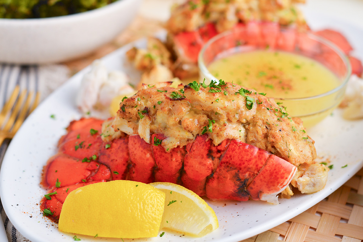 straight on shot of platter of stuffed lobster tails with lemon wedges and melted butter