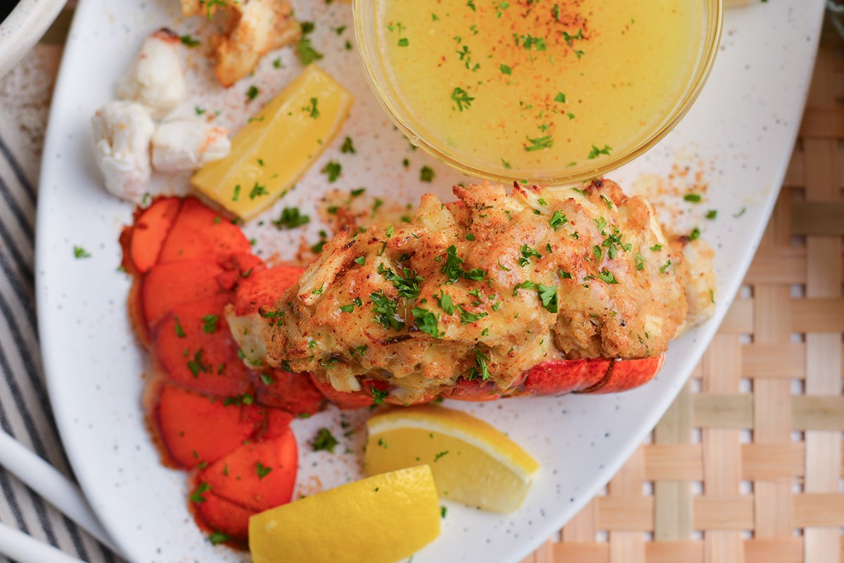 overhead shot of stuffed lobster tail on plate with melted butter and lemon