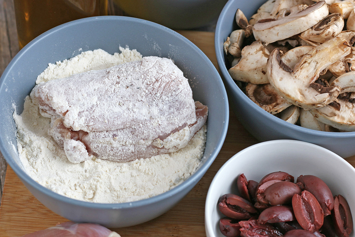 angled shot of raw chicken in bowl of flour