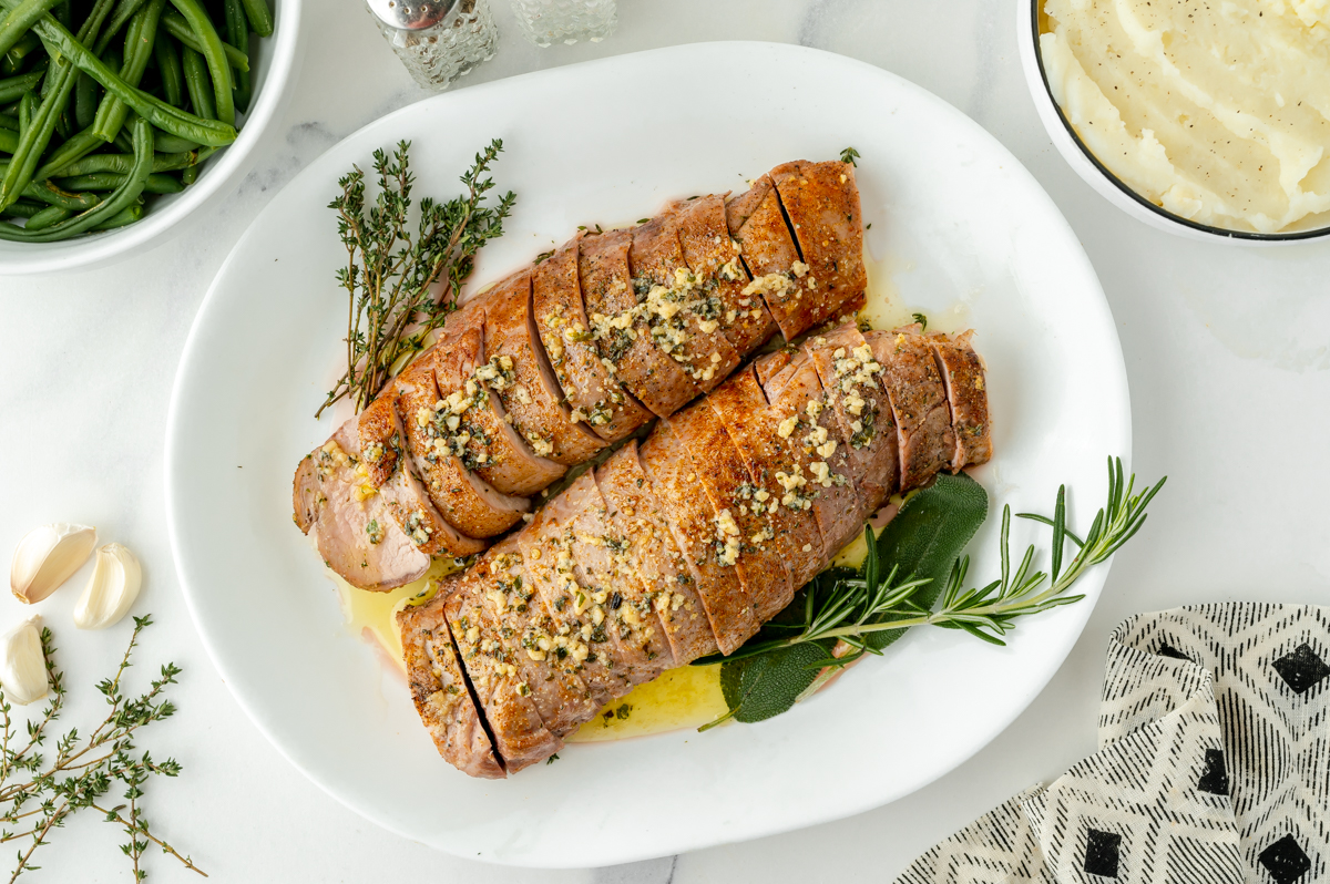 overhead shot of sliced pork tenderloin medallions on platter with herbs